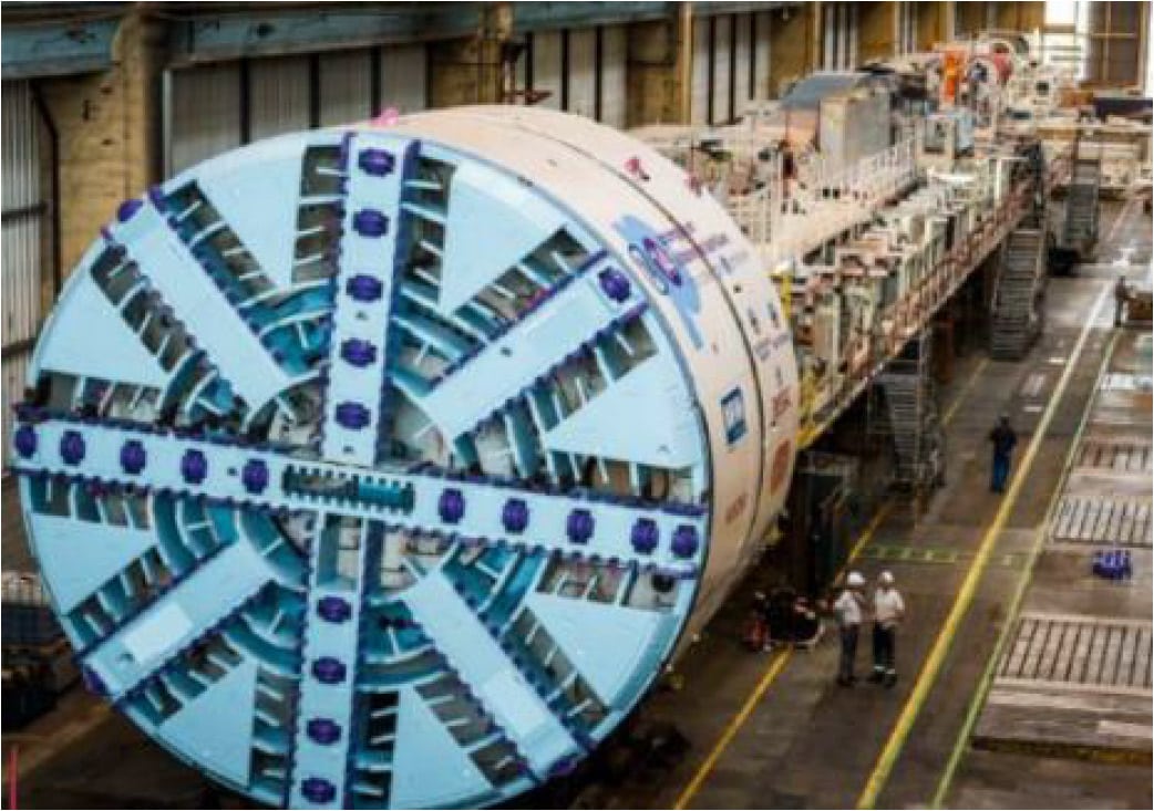 Two workers standing next to a tunnel boring machine.