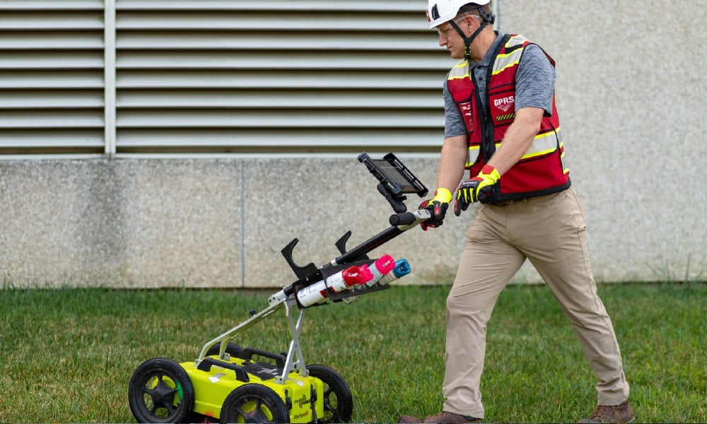 A GPRS Project Manager pushing a ground penetrating radar cart along grass.