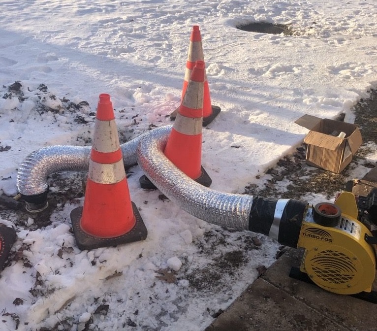 A smoke testing blower attached to sewer cleanouts in the snow.