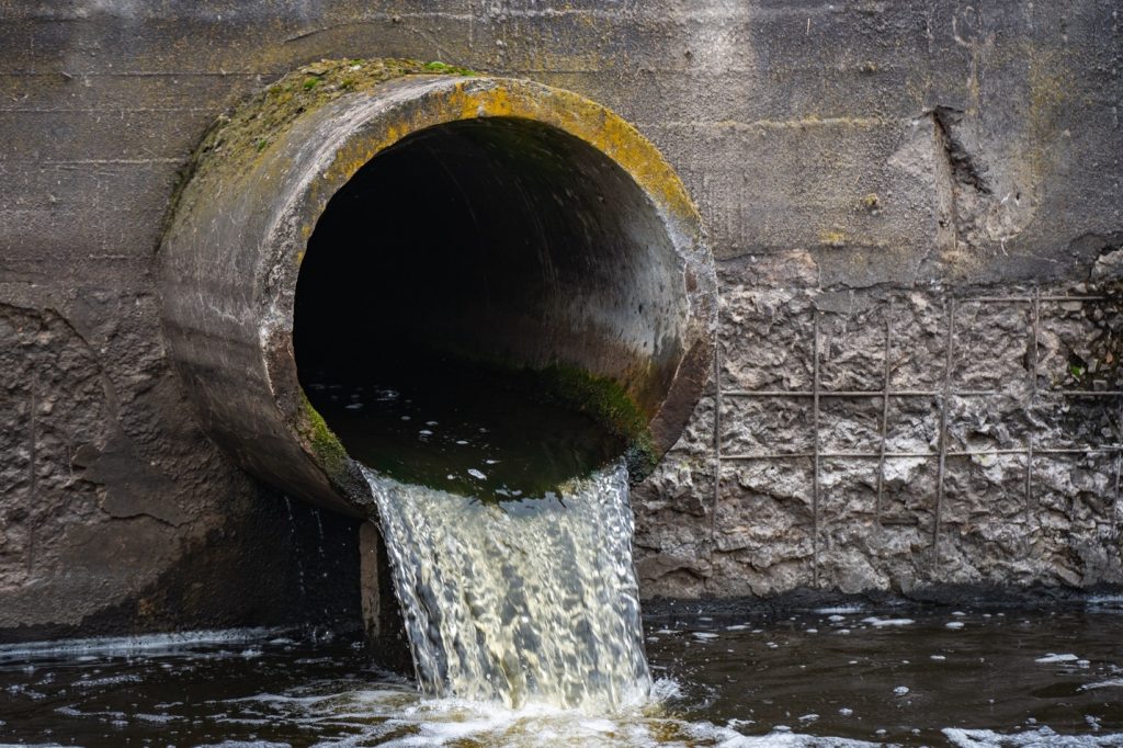 Water drains out of a sewer pipe into a body of water.