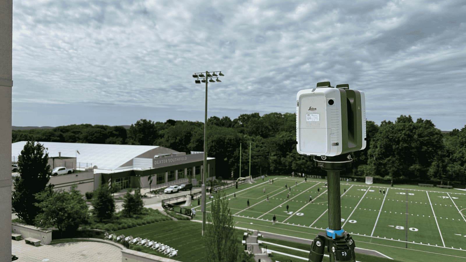 A 3D laser scanner situated above a football field with people on it.