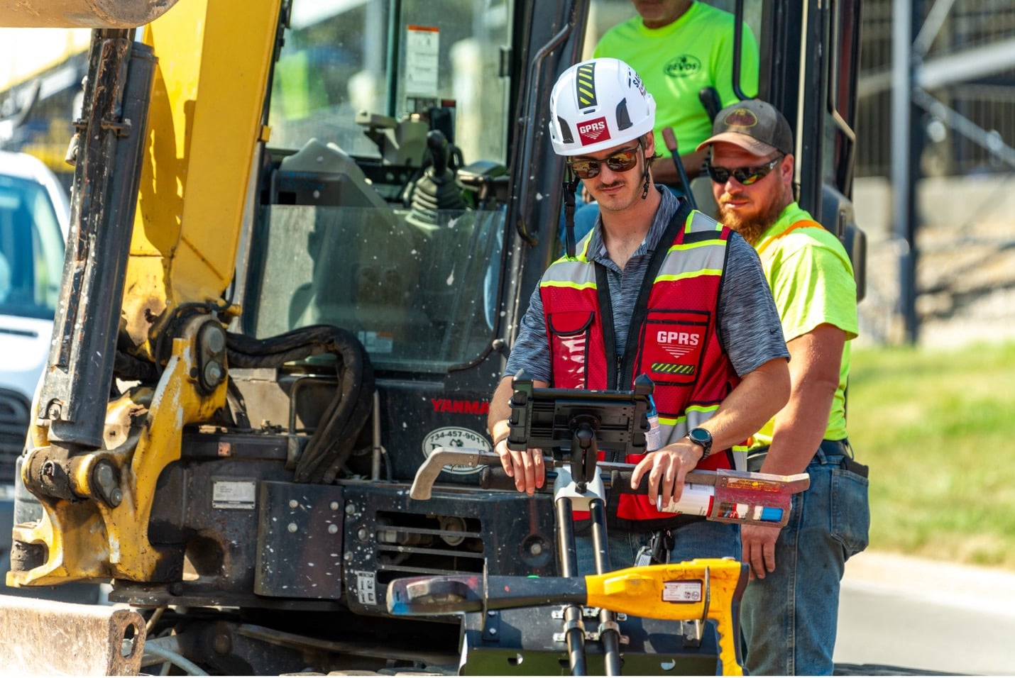 Construction workers watch a GPRS Project Manager pushing a ground penetrating radar cart on a construction site.