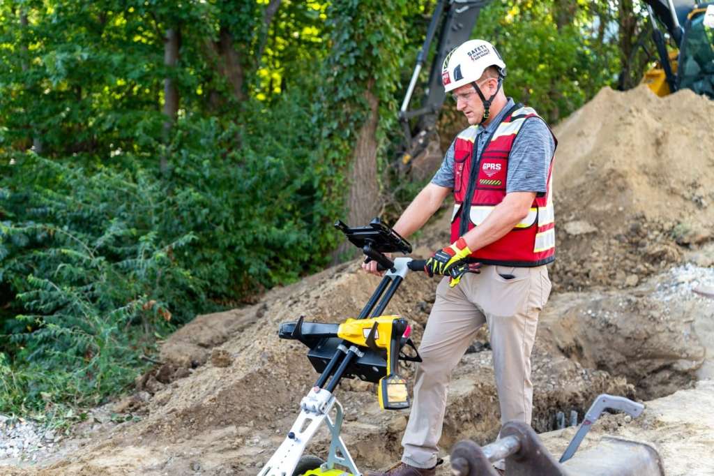 A GPRS Project Manager pushes a ground penetrating radar utility locating cart across an active job site.