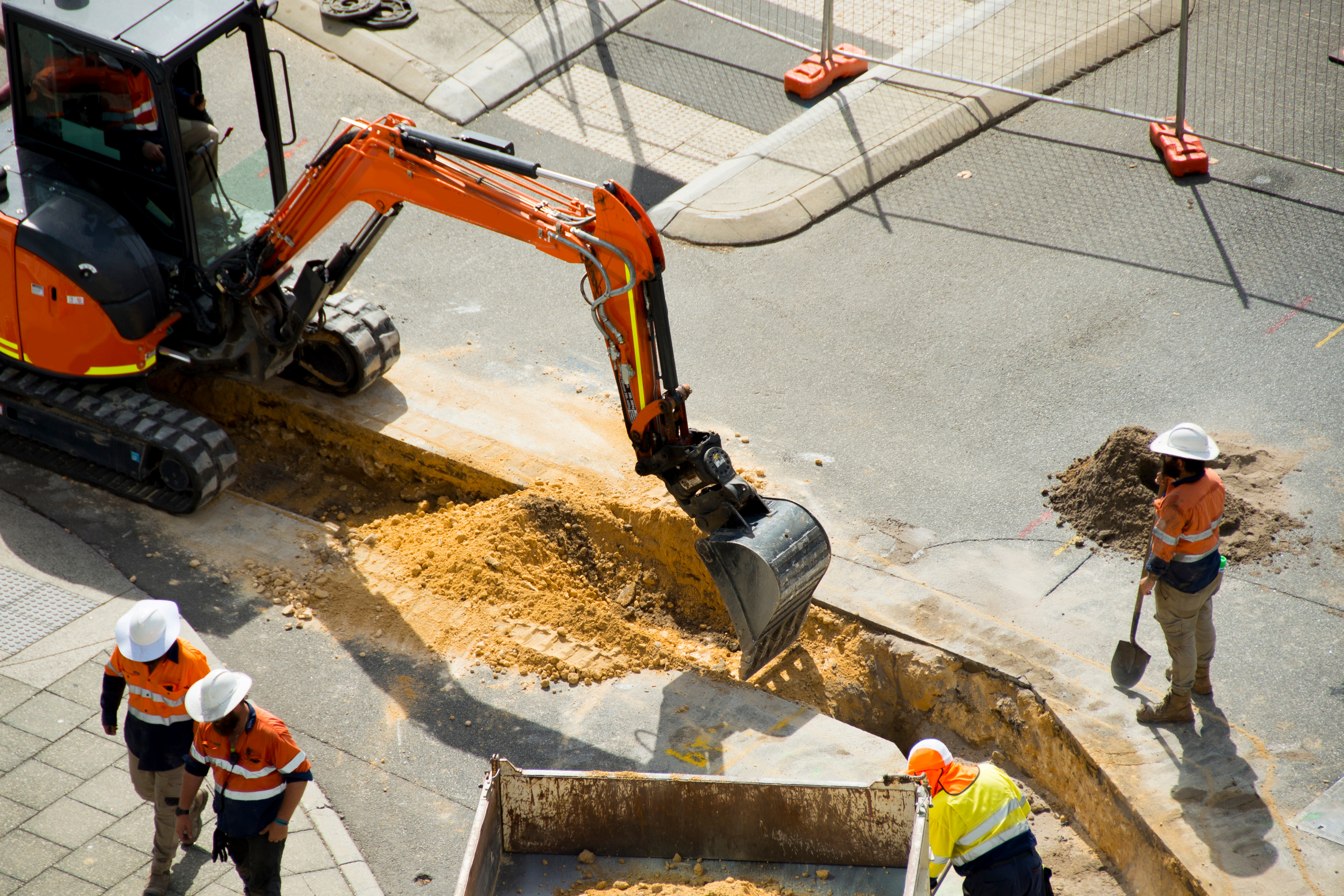 Overhead view of workers digging a trench in a road with an excavator.