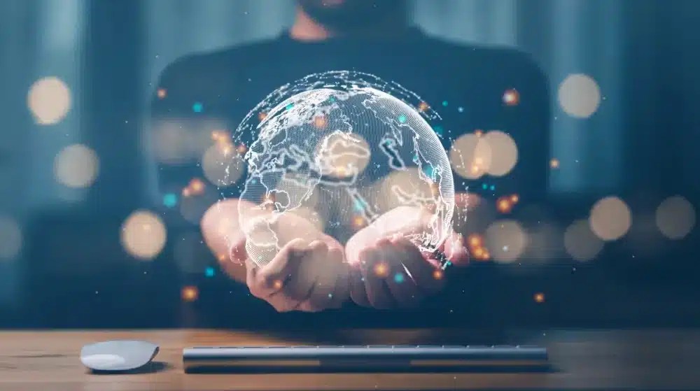 Person holding a digital hologram of the Earth above a desk, symbolizing global data connectivity, interactive mapping, and digital asset management.