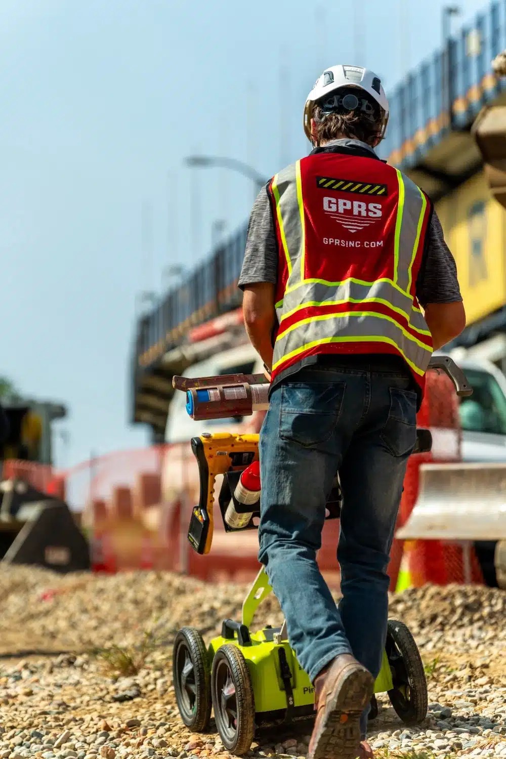 A GPRS Project Manager pushes a ground penetrating radar cart across a construction site.