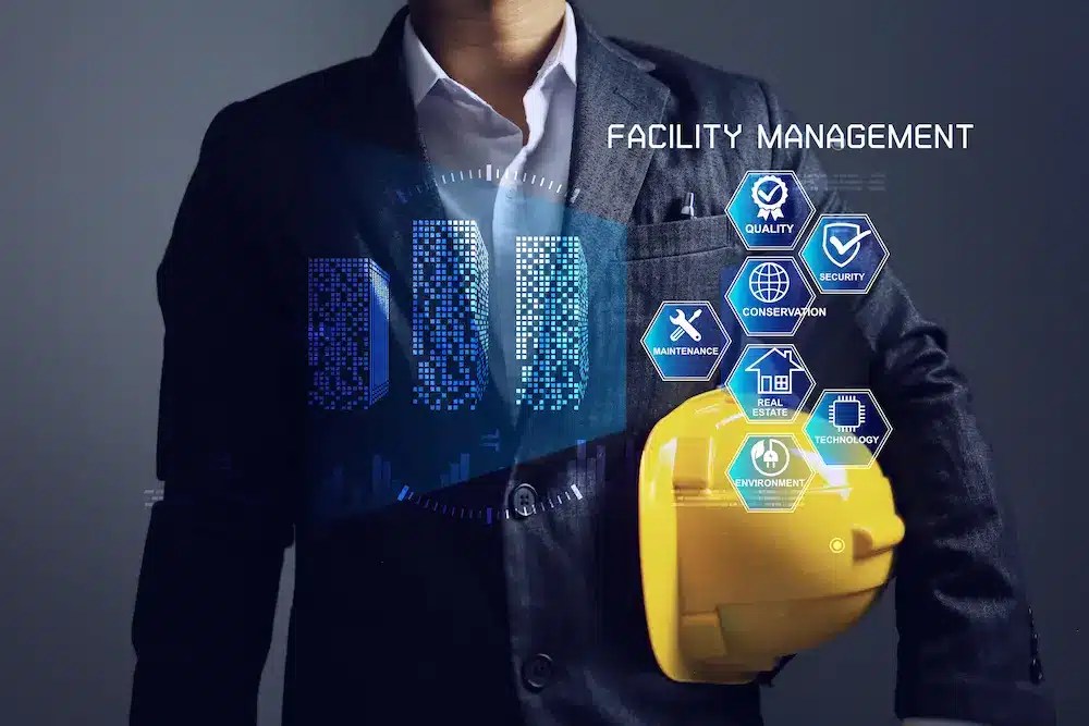 A person in a suit holding a yellow hard hat with holographic icons and text related to facility management displayed around the person.