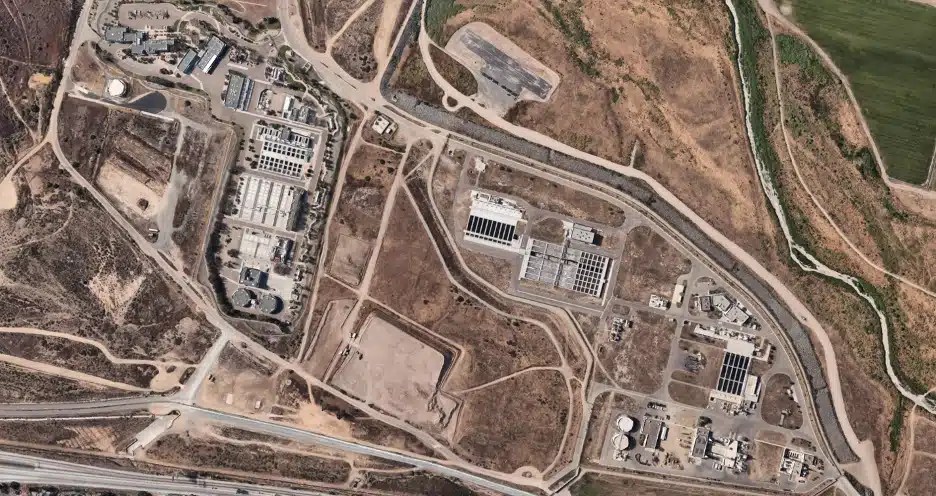 Aerial image showing the South Bay International Wastewater Treatment Plant, including multiple buildings, roads, and utility infrastructure within the facility grounds.
