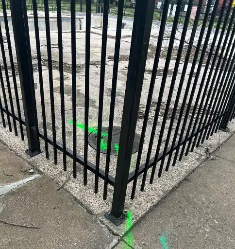 Bright green spray paint identifying the location of buried utilities on a sidewalk with fencing installed on top.
