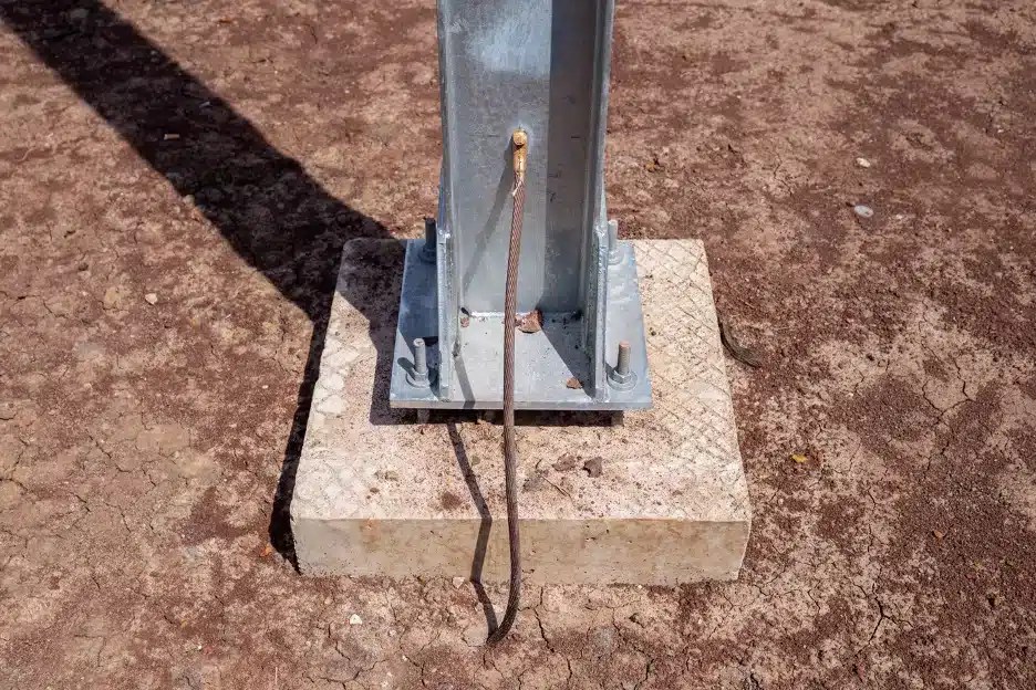 A copper grounding wire coming from the ground and connecting to a steel beam on a concrete footer.